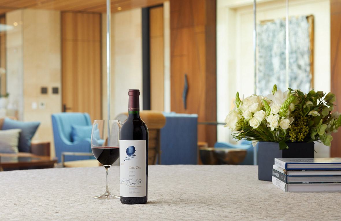 A bottle of Opus One 2018 next to a wine glass and floral arrangement in the Partners' Room.