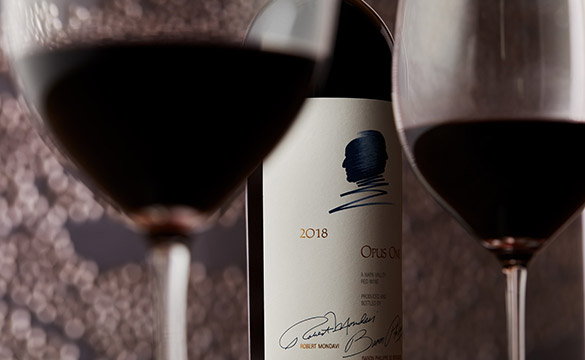 A bottle of Opus One 2018 with two wine glasses and an artistic backdrop